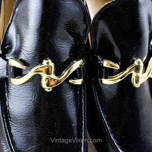 May include: A pair of black leather loafers with gold buckles. The loafers have a shiny finish and a classic design.