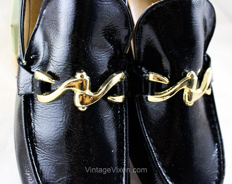 May include: A pair of black leather loafers with gold buckles. The loafers have a shiny finish and a classic design.