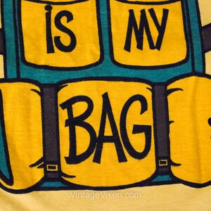 Puede incluir: Camiseta amarilla con un gr&aacute;fico de una mochila azul y verde con el texto "This is my bag".