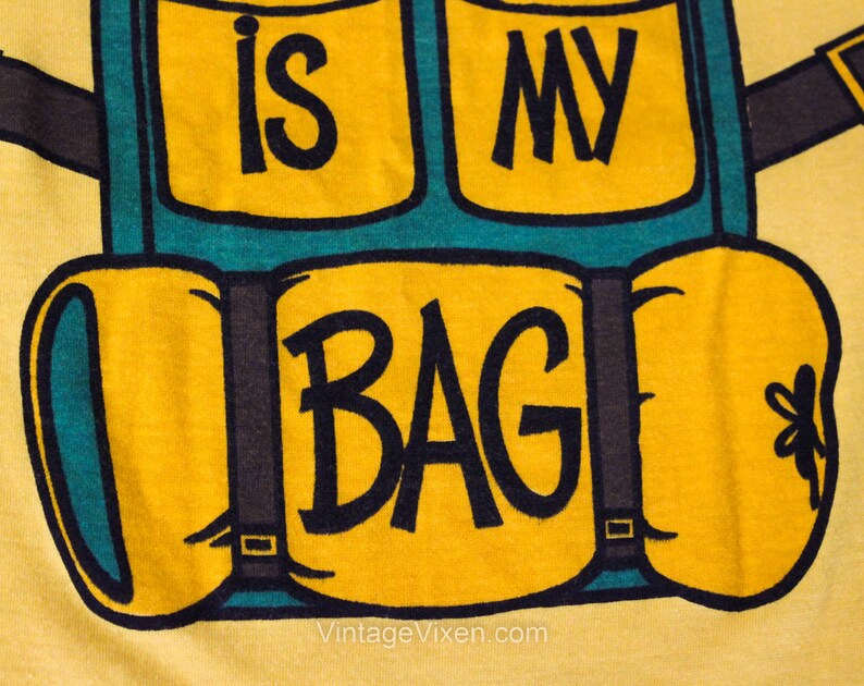 Puede incluir: Camiseta amarilla con un gr&aacute;fico de una mochila azul y verde con el texto "This is my bag".