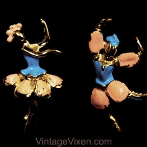 May include: Two gold-tone ballerina brooches with pink and blue enamel. One ballerina is in a blue dress with a pink tutu and the other is in a pink dress with a blue tutu.