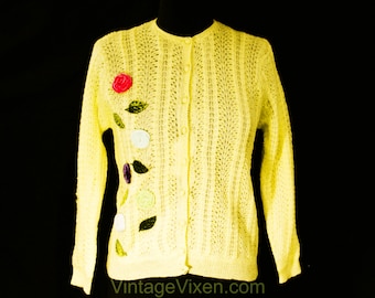 May include: A yellow knitted cardigan with a floral design. The cardigan has a button-up front and long sleeves. The flowers are embroidered in various colors, including pink, green, and purple.