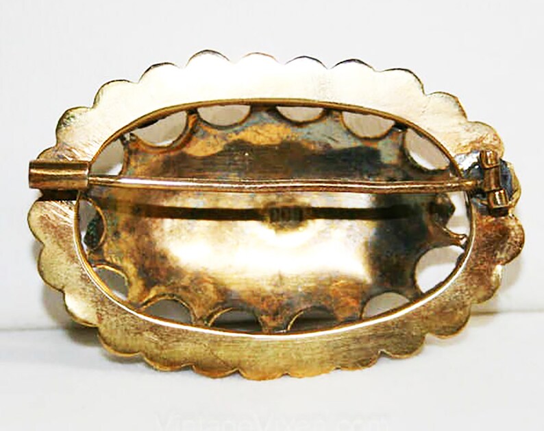 Puede incluir: Broche ovalada de oro con un borde festoneado y un dise&ntilde;o detallado. La broche tiene un cierre de pin y cierre en la parte posterior.
