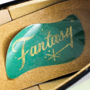 May include: Close-up of the inside of a black shoe with a green label that says "Fantasy" in gold lettering.