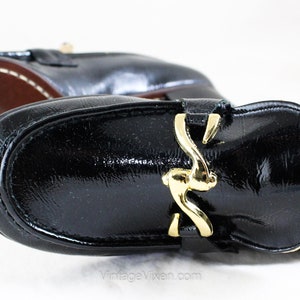 May include: Black leather loafers with a gold buckle. The loafers have a pointed toe and a low heel.