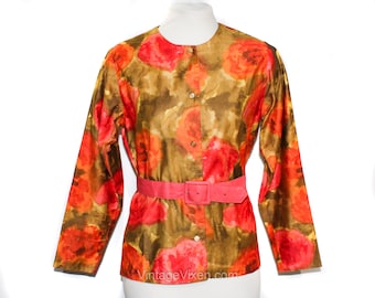 Puede incluir: Una blusa vintage de estampado floral con fondo marrón y flores rojas y naranjas. La blusa tiene un cierre de botones en la parte delantera y un cinturón rosa.