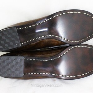 May include: A pair of brown leather shoes with a white stitch detail around the sole. The shoes have a textured rubber sole.