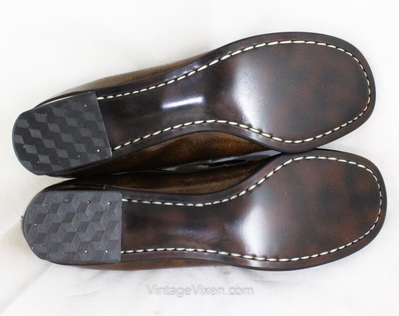 May include: A pair of brown leather shoes with a white stitch detail around the sole. The shoes have a textured rubber sole.