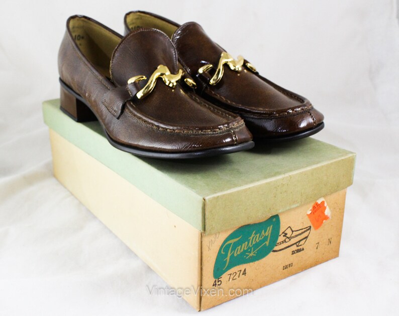 May include: Brown leather loafers with a gold buckle and a low heel. The shoes are in a box labeled "Fantasy" with the number 45 7274.