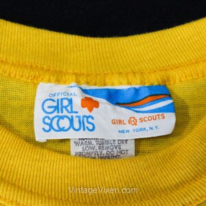 Puede incluir: Una etiqueta blanca con detalles azules y naranjas que dice "OFFICIAL GIRL SCOUTS NEW YORK, NY."