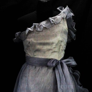 May include: A one-shoulder, gray tulle dress with a ruffled neckline and a gray satin sash.