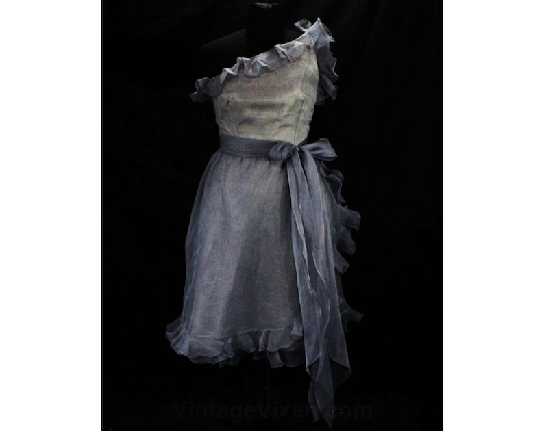 May include: A light blue one-shoulder dress with a ruffled neckline and a matching sash. The dress is made of a sheer fabric and has a flowing silhouette.