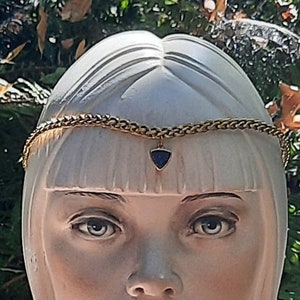 Peut inclure: Un buste en porcelaine blanche d'une femme portant un bandeau en chaîne dorée avec un pendentif en pierre bleue. Le buste porte une écharpe de couleur pêche clair.