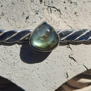 May include: A silver bracelet with a twisted design and three teardrop-shaped green gemstones.