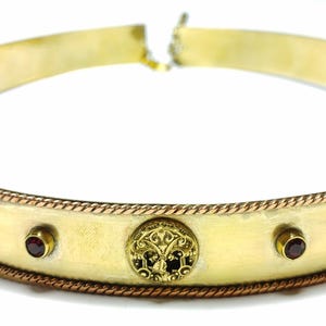 Peut inclure: Une couronne en métal doré avec une bordure en forme de corde et cinq pierres précieuses rouges. La couronne est décorée de cinq médaillons circulaires aux motifs complexes.