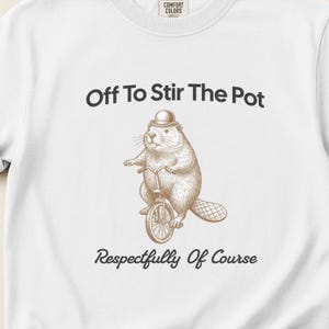May include: White sweatshirt featuring the text "Off To Stir The Pot" above a beaver riding a bicycle illustration, with "Respectfully Of Course" below. The beaver is wearing a bowler hat.