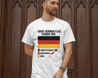 May include: White t-shirt with a graphic of the German flag and text that reads "What German flag stands for:" with a black square, red rectangle, and yellow square below the flag. The squares are labeled "Dark Rye Bread", "Bratwurst", and "Beer" respectively.