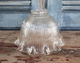 May include: A clear glass lampshade with a fluted design and a scalloped edge. The lampshade is sitting on a wooden surface.