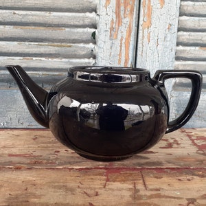 May include: A black ceramic teapot with a rounded body and a shiny glaze.