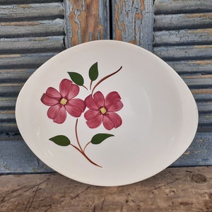 May include: White oval serving dish with a floral design. Two pink flowers with yellow centers and green leaves are painted on the dish.