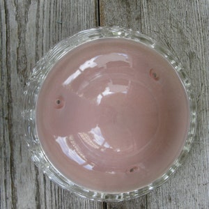 Puede incluir: Un cuenco de vidrio transparente con un interior rosa y un borde decorativo. El cuenco est&aacute; vac&iacute;o y se encuentra sobre una superficie de madera.