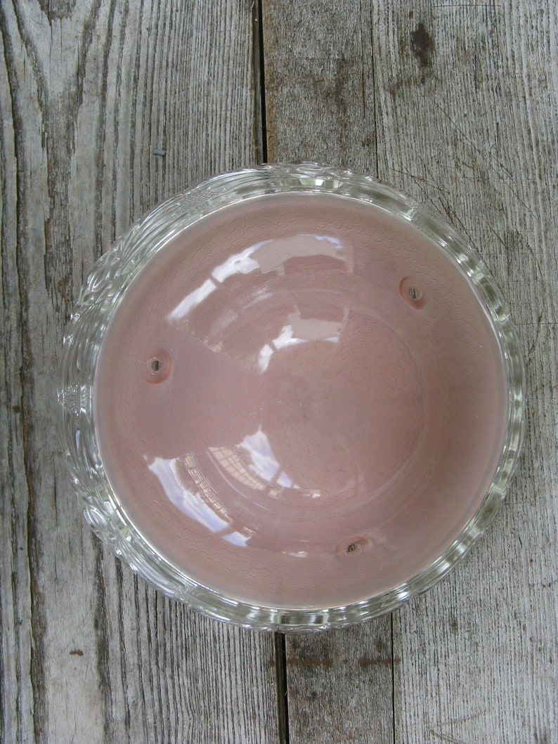 Puede incluir: Un cuenco de vidrio transparente con un interior rosa y un borde decorativo. El cuenco est&aacute; vac&iacute;o y se encuentra sobre una superficie de madera.