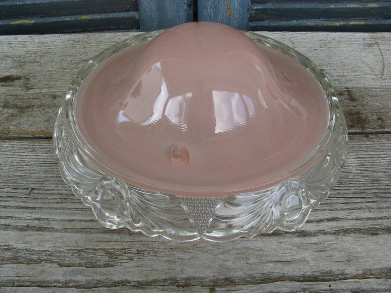 Puede incluir: Una l&aacute;mpara de techo de vidrio transparente con una pantalla de vidrio rosa y un borde decorativo festoneado.