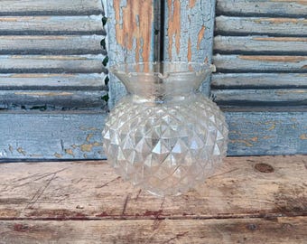 May include: Clear glass lampshade with a diamond pattern and ruffled edge. The lampshade is sitting on a weathered wooden surface in front of a blue shutter.