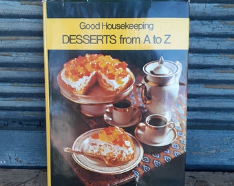 May include: A vintage cookbook titled "Good Housekeeping Desserts from A to Z" with a yellow and black cover. The cover features a cake on a stand, a teapot, cups, and a slice of cake on a plate. The background is a distressed blue wooden surface.