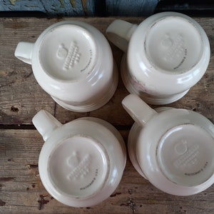 May include: Four white ceramic mugs with a floral design and the words "Pfaltzgraff USA" on the bottom.