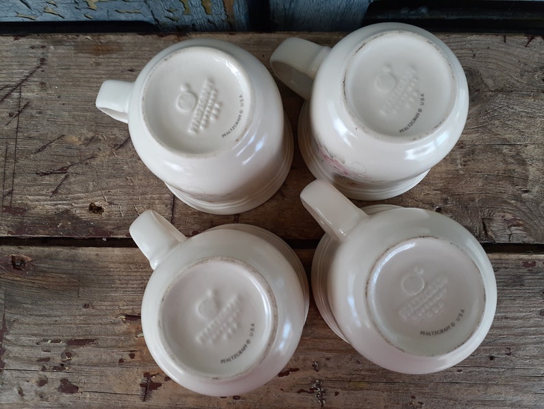 May include: Four white ceramic mugs with a floral design and the words "Pfaltzgraff USA" on the bottom.