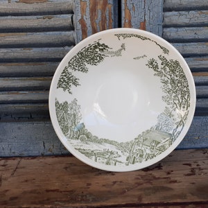 May include: A white ceramic bowl with a green and white design of a countryside scene. The bowl has a rim and a rounded bottom.