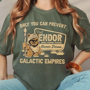 May include: Moss green t-shirt featuring the text "ONLY YOU CAN PREVENT" and a graphic of a bear-like creature holding a spear. The graphic includes the words "Visit Endor, Lunar Forest, Galactic Empires".
