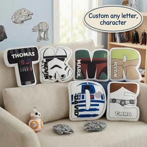 May include: Six letter-shaped scatter cushions featuring Star Wars character designs and personalised names. The cushions are shaped like the letters T, K, M, R, D, and E, displaying graphics of Darth Vader, a Stormtrooper, Boba Fett, and R2-D2.