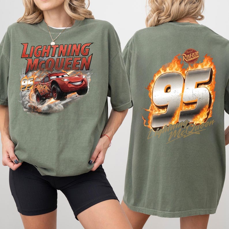 Op de afbeelding: Olijfgroen T-shirt met Lightning McQueen uit de film Cars. De afbeelding op de voorkant toont McQueen in de race met de tekst "Lightning McQueen" erboven. De achterkant van het shirt toont het nummer "95" in vlammen met de tekst "Lightning McQueen".