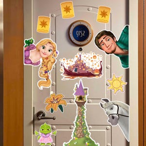 May include: A set of decorative wall decals featuring characters and scenes from the movie Tangled, including Rapunzel, Flynn Rider, Pascal, Maximus, a tall stone tower, a boat scene with floating lanterns, and a golden sun emblem.