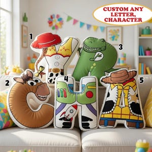 May include: Five plush letter-shaped cushions featuring character designs from Toy Story, including a Y with a cowgirl hat, a C shaped like a horse, an R with a green dinosaur, an H with space ranger details, and an A with a cowboy outfit.