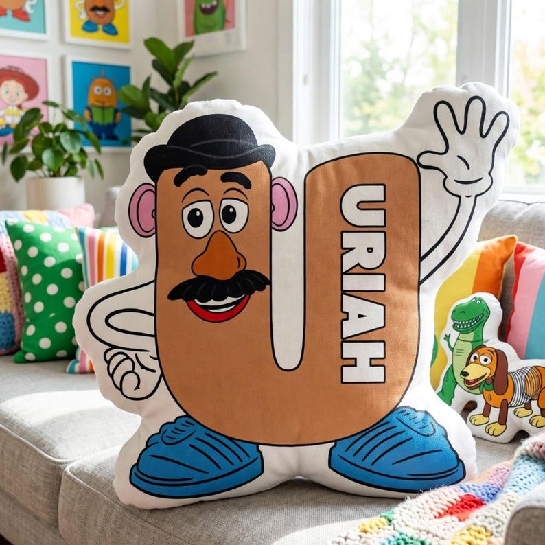 Puede incluir: Un gran coj&iacute;n blanco en forma de U con un dise&ntilde;o de personaje de dibujos animados. El personaje tiene una cara marr&oacute;n, un bigote negro y un sombrero negro. El nombre "URIAH" est&aacute; impreso verticalmente. Zapatos azules y una mano que saluda completan el dise&ntilde;o.