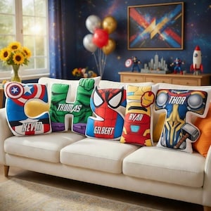 May include: Five custom letter-shaped throw pillows arranged on a sofa. The pillows feature superhero-themed designs including Captain America, Hulk with the name Thomas, Spider-Man with the name Gilbert, Iron Man with the name Ryan, and Thor.