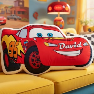 May include: A red plush pillow shaped like a race car, featuring the number 95 in yellow, blue eyes on the windshield, and the name David printed in white script on the hood. The design includes black tires and yellow lightning bolt accents.