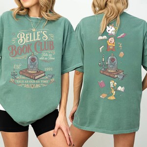May include: Green t-shirt with "Belle's Book Club" graphic on the front, featuring a rose in a glass dome, books, and teacups. The back of the shirt has a similar design with animated characters and books. The text "Tale as old as Time" is also included.