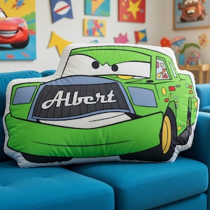 May include: A plush throw pillow shaped like a green cartoon race car with large eyes on the windshield. The front grille features the name Albert in white script lettering. The car design includes yellow wheels, black tires, and various colorful decals.