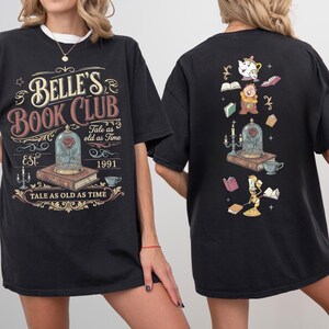 May include: Black t-shirt featuring the text "Belle's Book Club" with a rose in a glass dome graphic. The back of the shirt has a matching design with characters and books. The shirt's design includes the phrase "Tale as old as Time" and the year "1991".