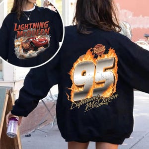 Op de afbeelding: Zwart sweatshirt met Lightning McQueen-ontwerp. De voorkant toont de tekst "Lightning McQueen" en een afbeelding van de rode raceauto. De achterkant heeft een grote "95" met vlammen en de tekst "Lightning McQueen".