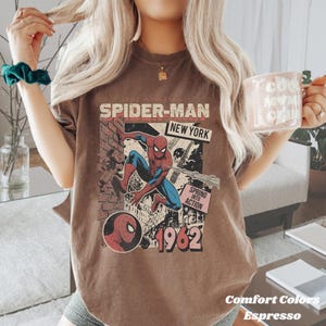 Op de afbeelding: Espresso-kleurig T-shirt met een vintage Spider-Man-afbeelding. Het ontwerp bevat de tekst "The Amazing Spider-Man New York" en "Spring into Action 1962". Onderdeel van de Comfort Colors collectie.
