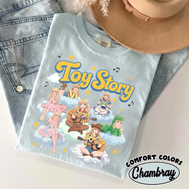 May include: A light blue t-shirt featuring the text Toy Story in yellow letters. The graphic displays multiple anime-style characters dressed in costumes inspired by the movie, including a cowgirl, a space ranger, and a dinosaur, all sitting on clouds.