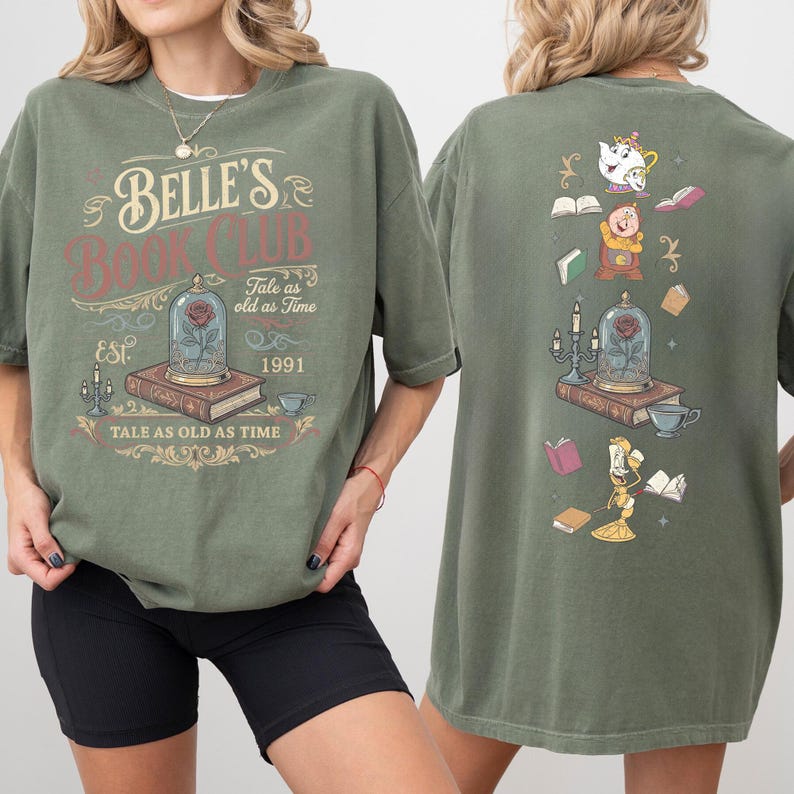 May include: Olive green t-shirt with "Belle's Book Club" graphic. The front design features a rose in a glass dome, books, and text. The back has a similar design with characters and books. "Tale as old as time" is also printed on the shirt.