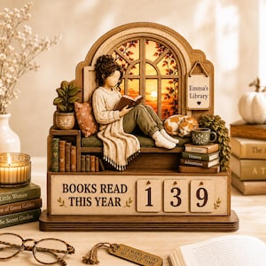 Peut inclure: Un calendrier de bureau en bois représentant une scène miniature d'une personne lisant près d'une fenêtre, avec une plaque Emma's Library et un compteur Books Read This Year affichant 139. Inclut un petit chat, des livres et une étiquette.