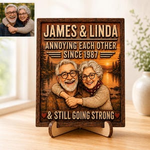 Può includere: Una targa rettangolare in legno con un'illustrazione personalizzata di una coppia anziana con occhiali. Il testo recita: JAMES & LINDA, ANNOYING EACH OTHER SINCE 1987, & STILL GOING STRONG. Lo sfondo raffigura un lago, alberi e un tramonto.