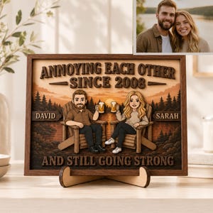 May include: A rectangular wooden wall art piece featuring a layered 3D illustration of a couple sitting in chairs at sunset, holding beer mugs. The text reads: ANNOYING EACH OTHER SINCE 2008, DAVID, SARAH, AND STILL GOING STRONG. Includes a photo insert.